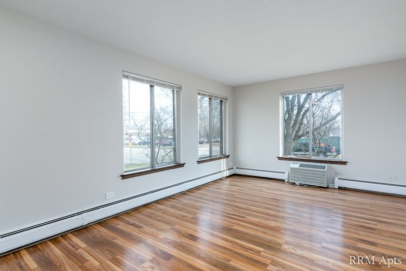 Living room with hardwood floor, three windows and a wall air conditioner, 4th and Broadway apartment 1A