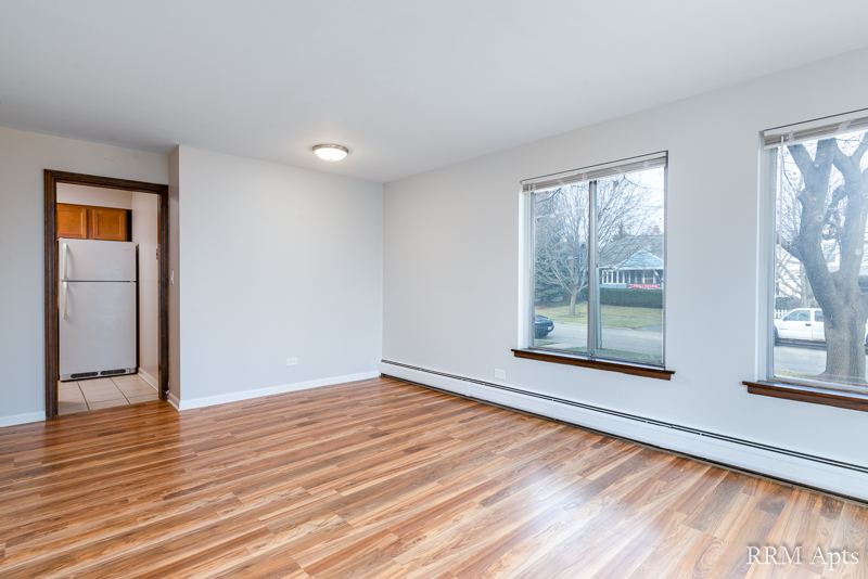 Living room with hardwood floor, corner windows and a doorway to the kitchen, 4th and Broadway apartment 1A