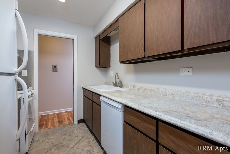 Kitchen with dark wood cabinets, white dishwasher, marble-look counter and hall doorway, 4th and Broadway apartment 1B