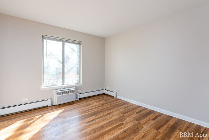 Bedroom with wood floor, one window, baseboard radiator and a wall air conditioner, 4th and Broadway apartment 1B