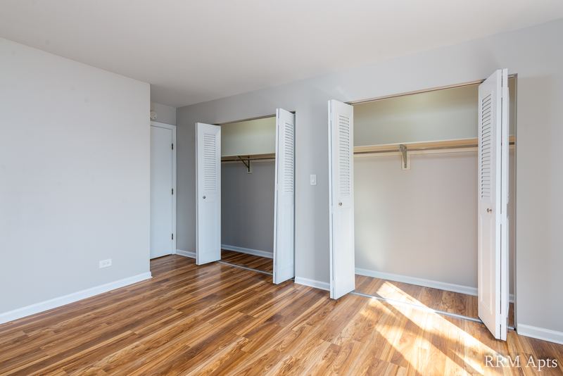 Bedroom with wood floor, two open bifold closets and a white door, 4th and Broadway apartment 1B