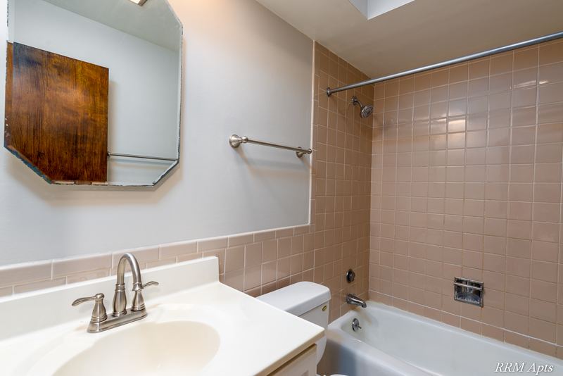 Bathroom with beige tile tub surround, white vanity and a mirrored medicine cabinet, 4th and Broadway apartment 2A