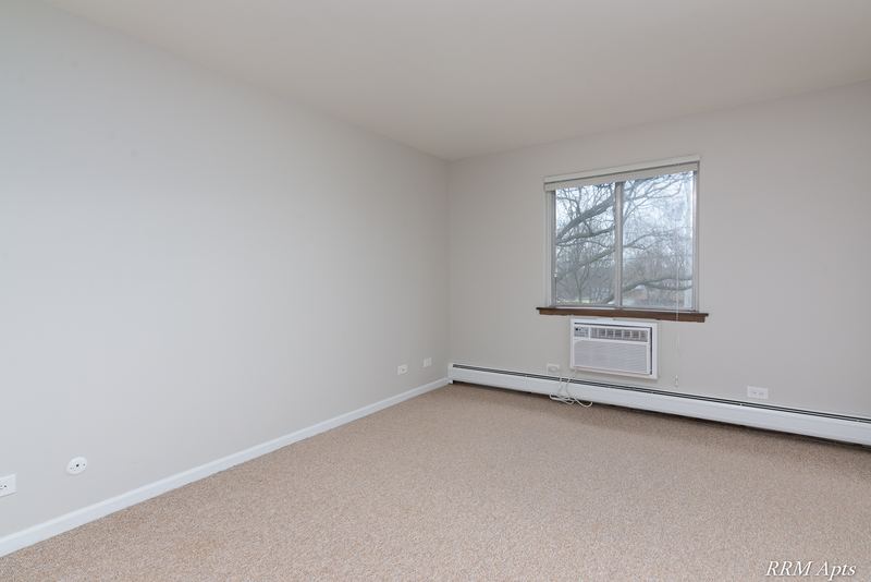 Carpeted bedroom with a window on the right wall, wall air conditioner and baseboard radiator, 4th and Broadway apartment 2A