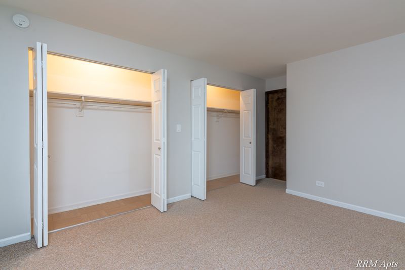 Carpeted bedroom with two open bifold closets and a doorway to the hall, 4th and Broadway apartment 2A