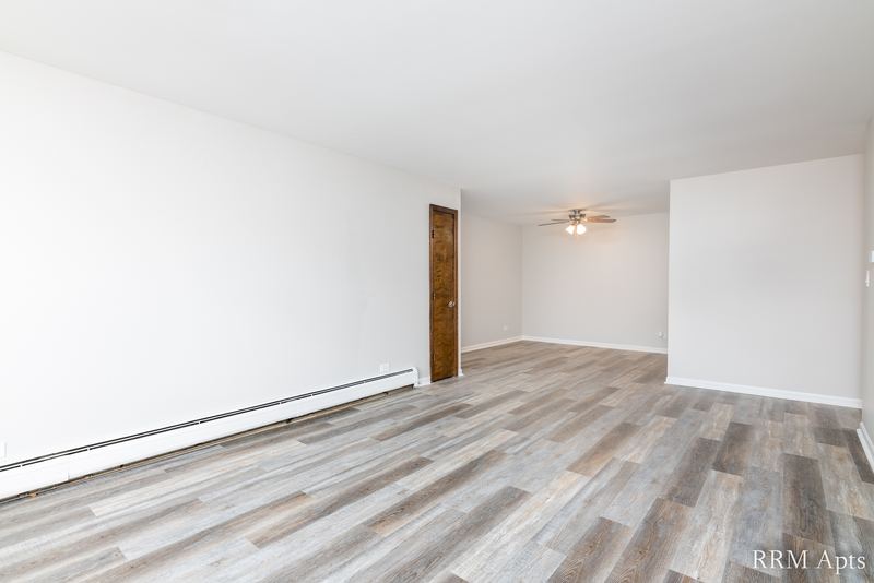 Living room with gray wood-look floor, ceiling fan and a doorway to the hall, 4th and Broadway apartment 2B
