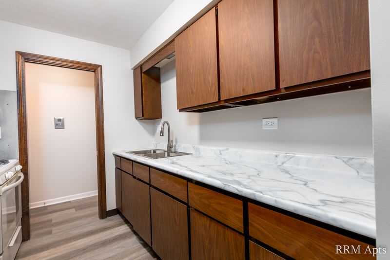Kitchen with dark wood cabinets, marble-look counter, stainless sink and a doorway to the hall, 4th and Broadway apartment 2B