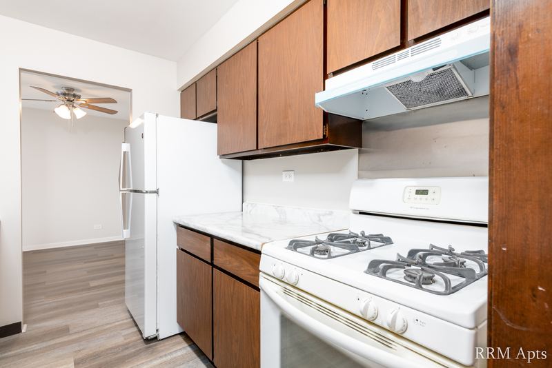 Kitchen with white gas stove, white refrigerator, dark wood cabinets and living room beyond, 4th and Broadway apartment 2B