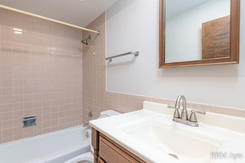 Bathroom with beige tile tub surround, white vanity, chrome faucet and a wood-framed mirror, 4th and Broadway apartment 2B