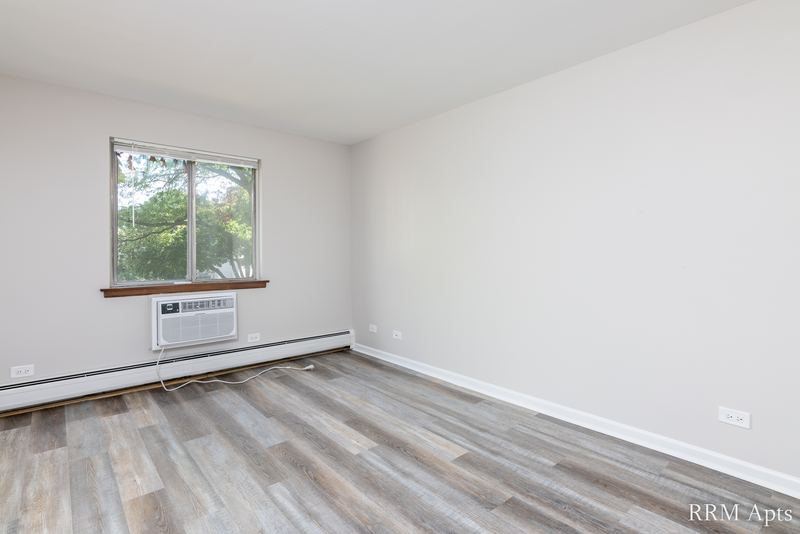 Bedroom with gray wood-look floor, one window and a wall air conditioner below it, 4th and Broadway apartment 2B