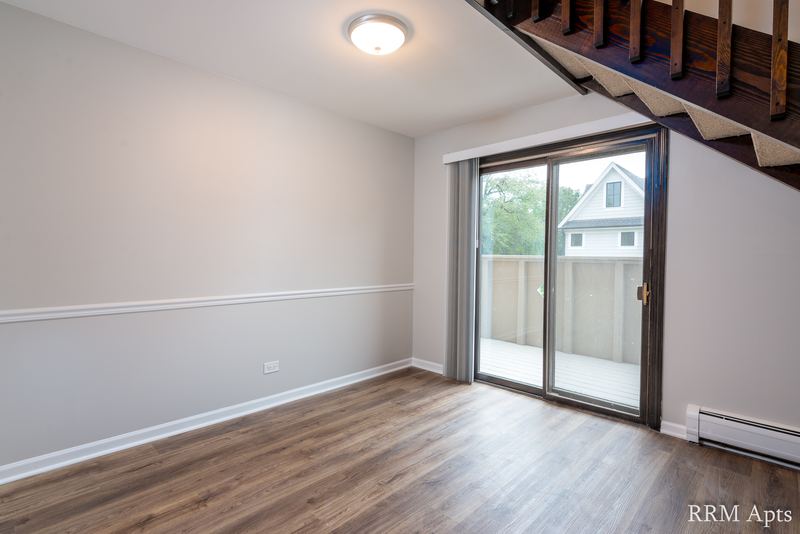 Living room with wood floor, sliding glass door to a balcony and an open staircase overhead, 4th and Broadway apartment 2C