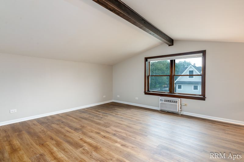 Upper-level room with wood floor, sloped ceiling with a beam and a wall air conditioner, 4th and Broadway apartment 2C
