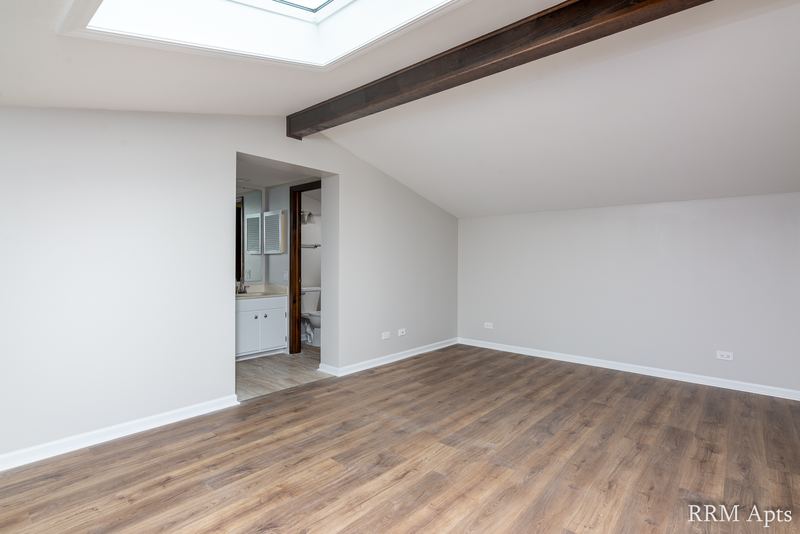 Upper-level room with wood floor, skylight, sloped ceiling and a doorway to the bathroom, 4th and Broadway apartment 2C