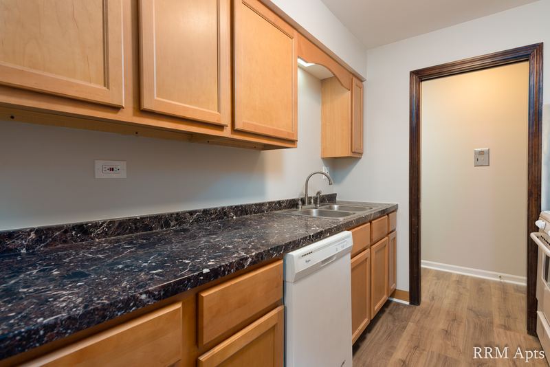 Kitchen with oak cabinets, dark granite-look counter, white dishwasher and hall doorway, 4th and Broadway apartment 2C