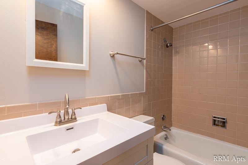 Bathroom with beige tile tub surround, white vanity sink and a mirrored medicine cabinet, 4th and Broadway apartment 2C