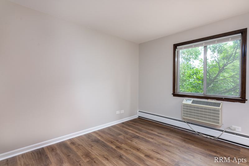 Bedroom with wood floor, a window on the right wall, wall air conditioner and radiator, 4th and Broadway apartment 2C