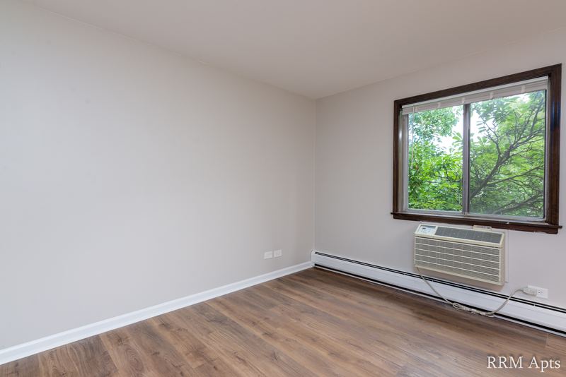 Bedroom with wood floor, one window with wall air conditioner and a sloped ceiling, 4th and Broadway apartment 2C