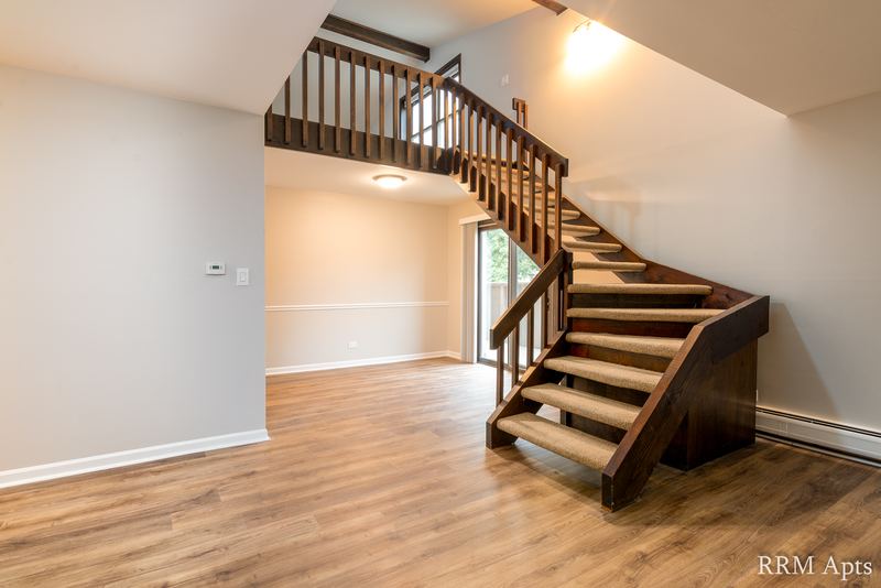 Living room with wood floor and an open wood staircase with railing to the upper level, 4th and Broadway apartment 2C