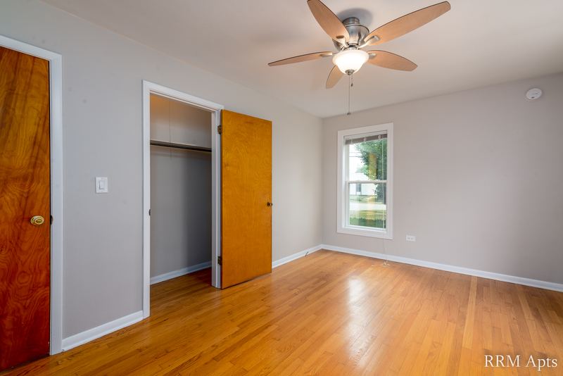 Bedroom with wood floor, ceiling fan, one window and an open closet beside a wood door, Austin Avenue apartment 116 A