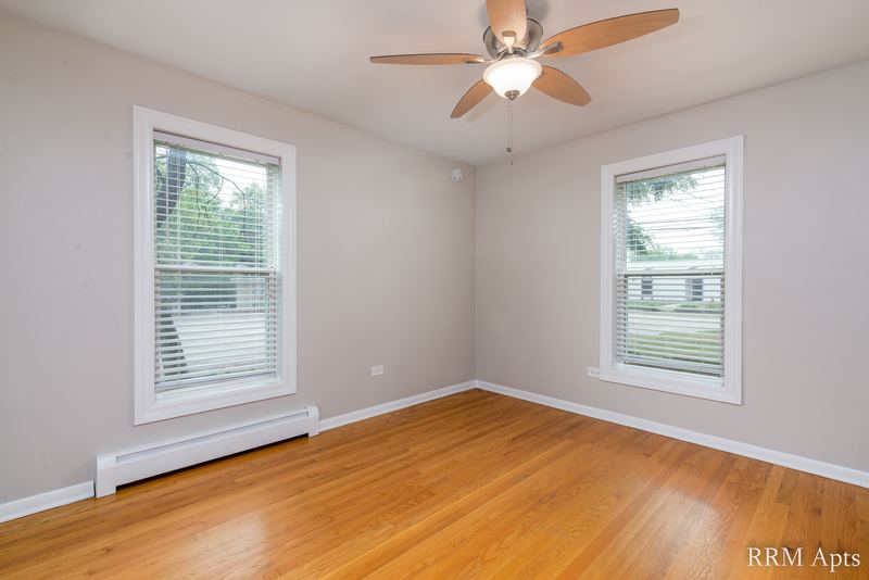 Bedroom with wood floor, ceiling fan, two windows and baseboard radiator, Austin Avenue apartment 116 A