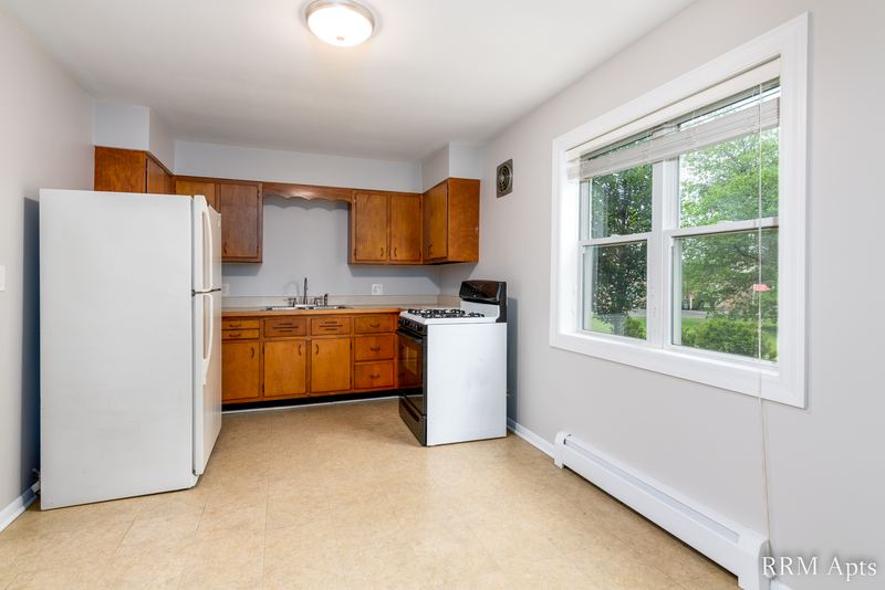 Kitchen with oak cabinets, white refrigerator, white stove, beige floor and a window, Austin Avenue apartment 118 A
