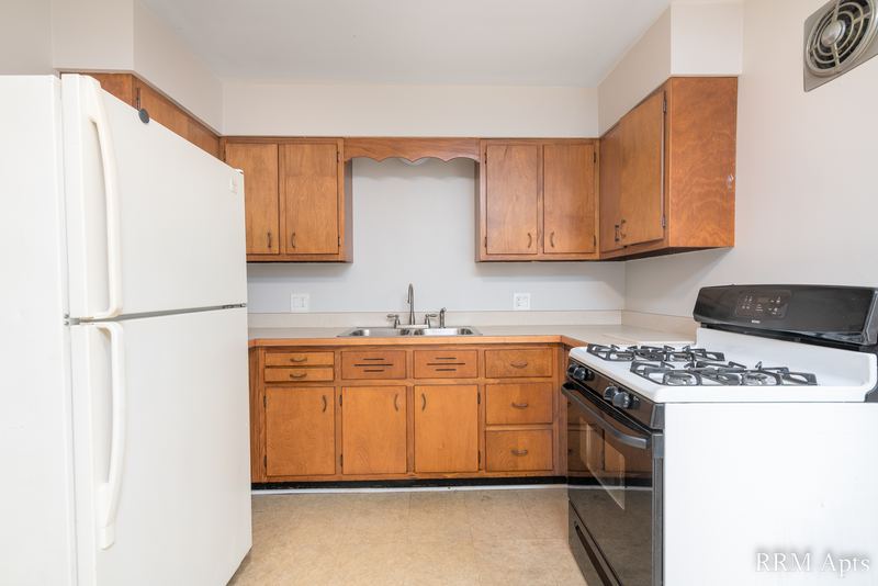 Kitchen with oak cabinets, white refrigerator and a black-and-white gas stove, Austin Avenue apartment 118 A