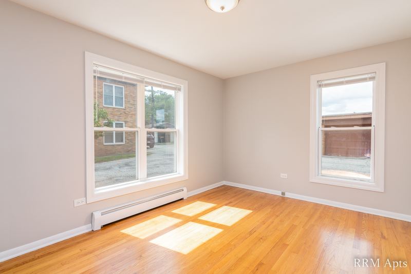 Bedroom with wood floor, two windows with sunlight on the floor and a baseboard radiator, Austin Avenue apartment 118 A