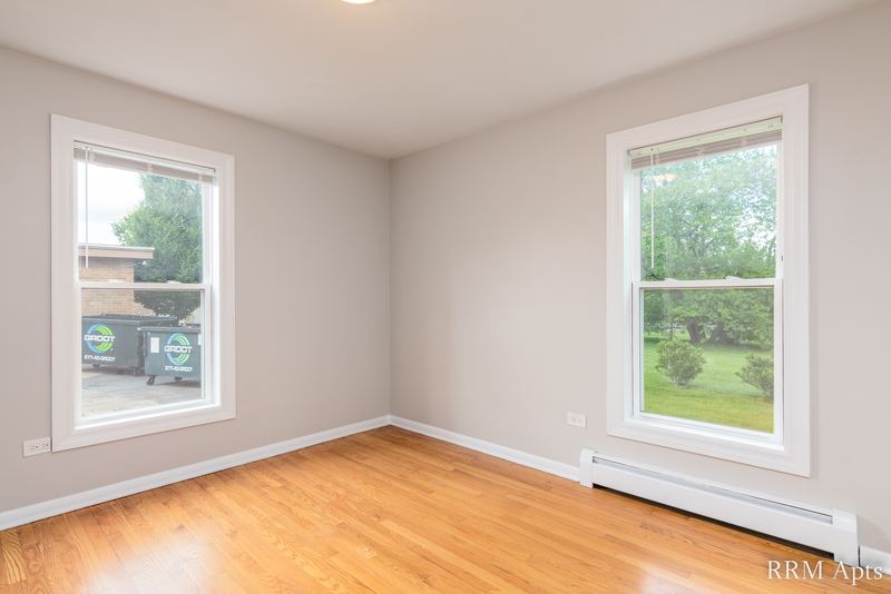 Bedroom with wood floor, two windows looking out at trees and a baseboard radiator, Austin Avenue apartment 118 A