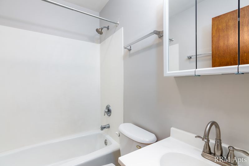 Bathroom with white tub and surround, toilet, white vanity and a wood medicine cabinet, Austin Avenue apartment 118 A