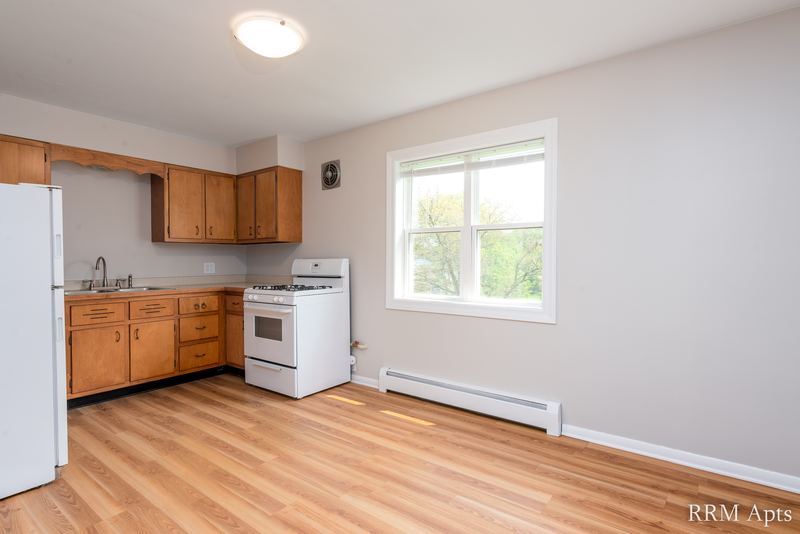 Kitchen with oak cabinets, white refrigerator, white stove, wood floor and a window, Austin Avenue apartment 118B