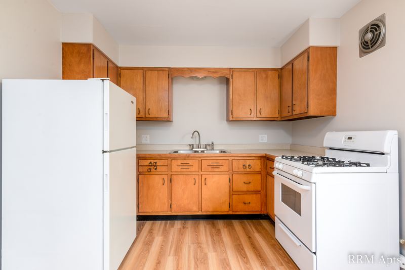 Kitchen with oak cabinets, white refrigerator, white gas stove and wood floor, Austin Avenue apartment 118B