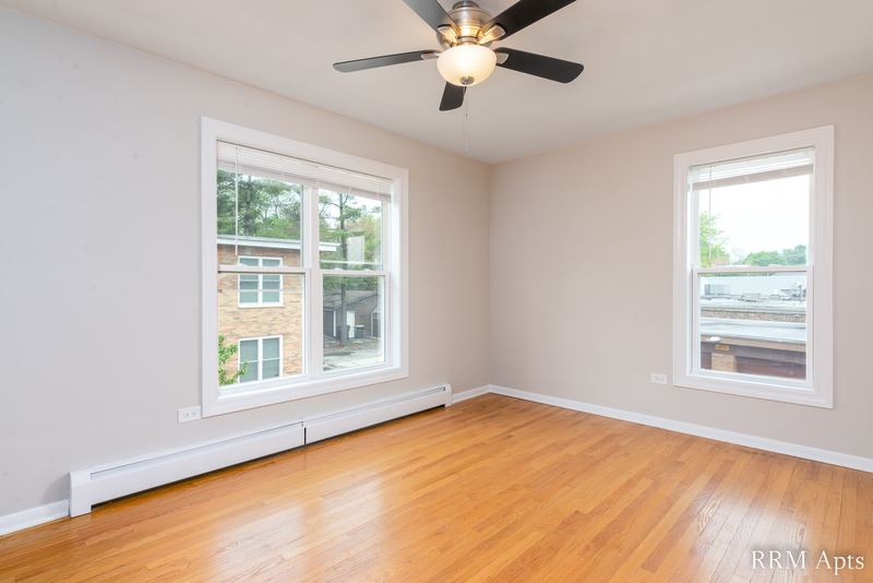 Bedroom with wood floor, ceiling fan, two windows and baseboard radiator, Austin Avenue apartment 118B