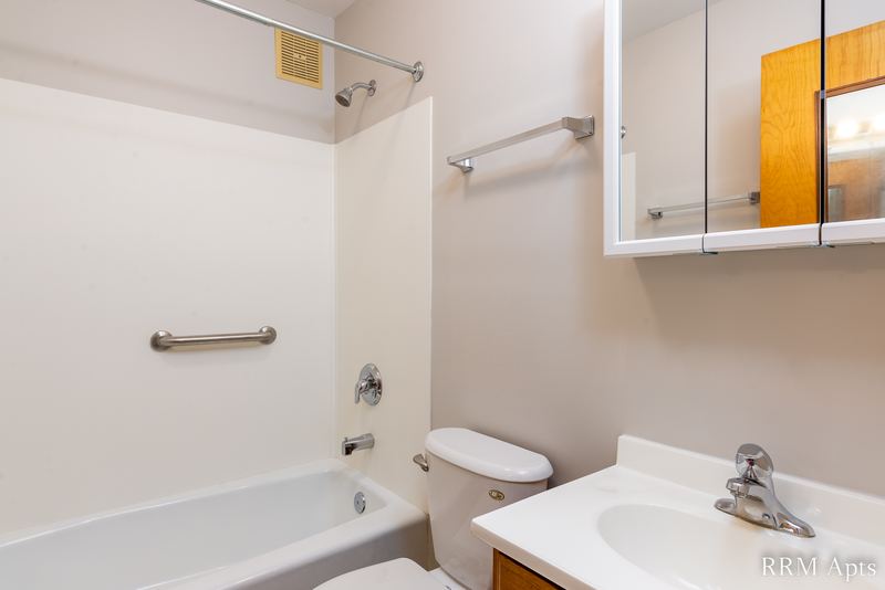 Bathroom with white tub and surround, toilet, white vanity sink and a wood medicine cabinet, Austin Avenue apartment 118B
