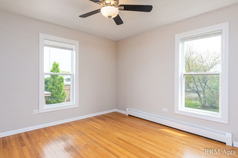 Bedroom with wood floor, ceiling fan and two windows looking out at trees, Austin Avenue apartment 118B
