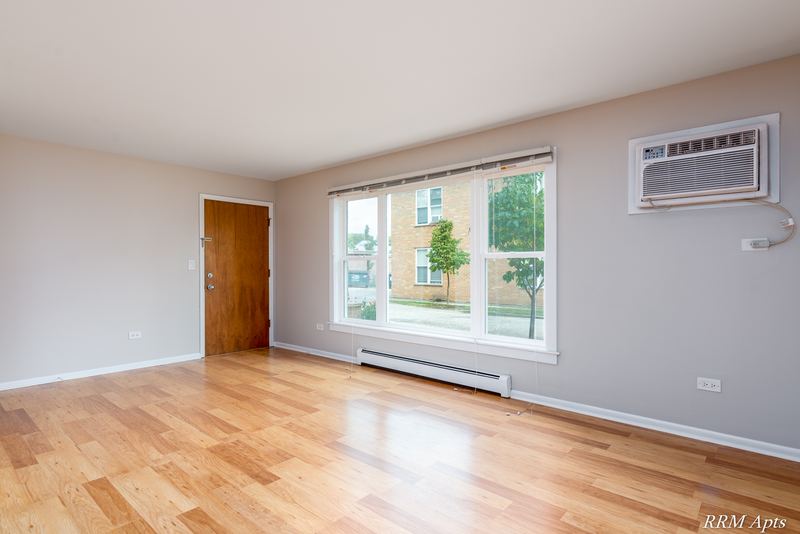 Living room with wood floor, a wide window, wall air conditioner and wood entry door, Austin Avenue apartment 120 A