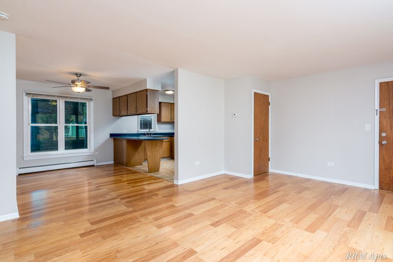 Living room with wood floor, ceiling fan and an open kitchen with dark counter beyond, Austin Avenue apartment 120 A