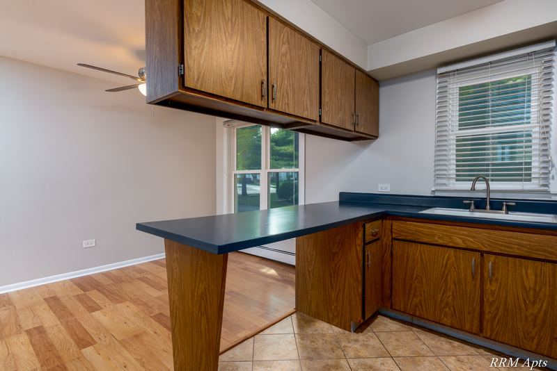Kitchen with dark wood cabinets, dark counter peninsula, a window with blinds and tile floor, Austin Avenue apartment 120 A