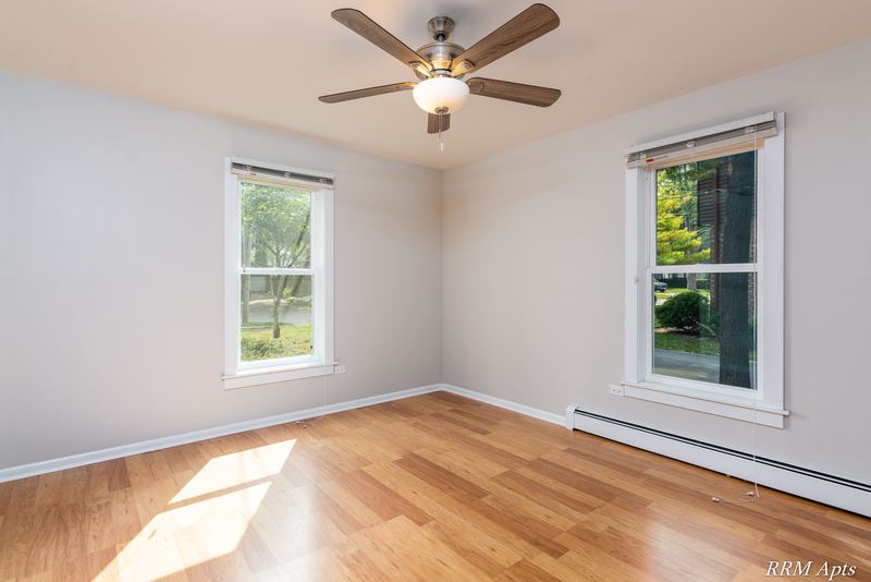 Bedroom with wood floor, ceiling fan, two windows and baseboard radiator, Austin Avenue apartment 120 A
