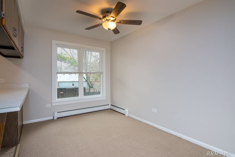Carpeted dining area with ceiling fan, one window and dark wood cabinets at the left, Austin Avenue apartment 122 B