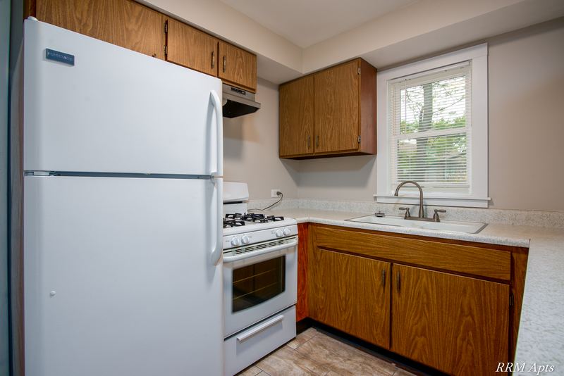 Kitchen with white refrigerator, white gas stove, dark wood cabinets and a window, Austin Avenue apartment 122 B