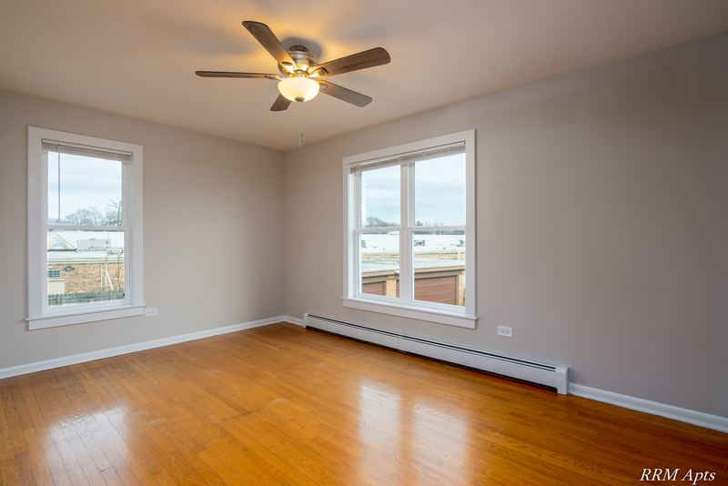Bedroom with wood floor, ceiling fan, two windows and baseboard radiator, Austin Avenue apartment 122 B