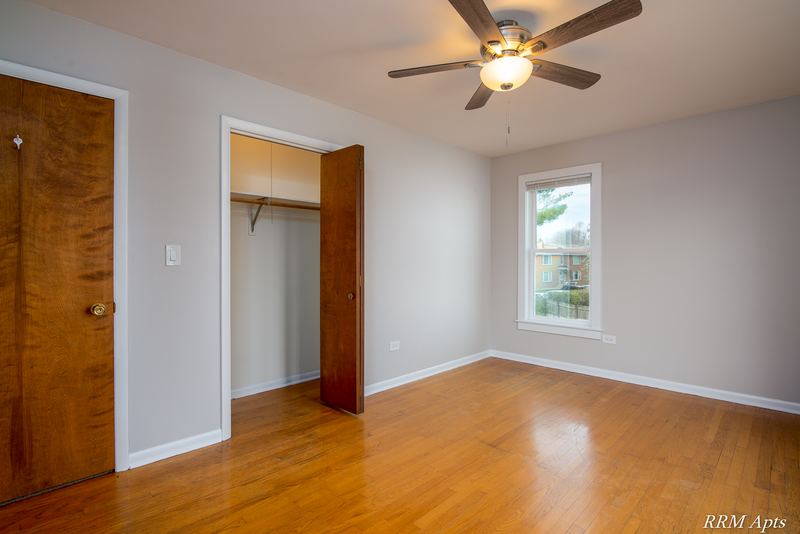 Bedroom with wood floor, ceiling fan, one window and an open closet beside a wood door, Austin Avenue apartment 122 B
