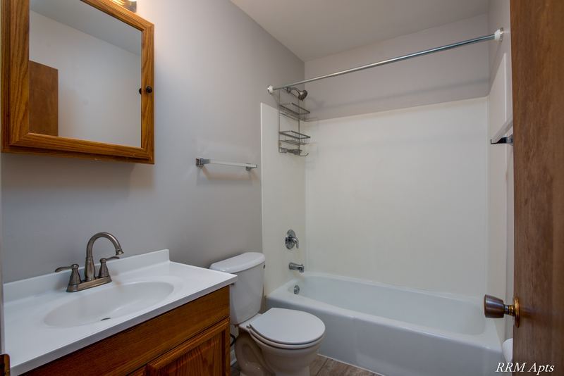 Bathroom with white tub and surround, toilet, white vanity and a wood medicine cabinet, Austin Avenue apartment 122 B
