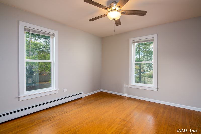Bedroom with wood floor, ceiling fan and two windows on adjoining walls, Austin Avenue apartment 122 B