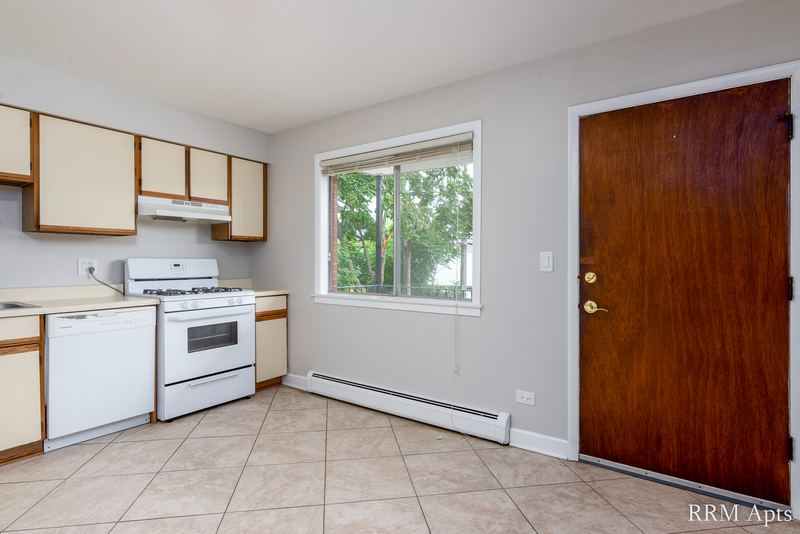 Kitchen with white cabinets, white stove and dishwasher, tile floor, window and a wood entry door, Cook Street apartment 4