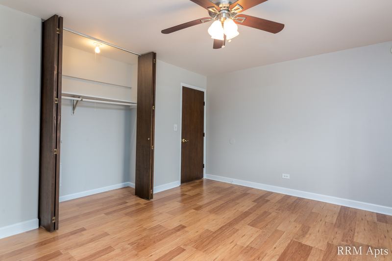 Bedroom with wood floor, ceiling fan, open closet with dark wood doors and a wood door on the right, Cook Street apartment 4