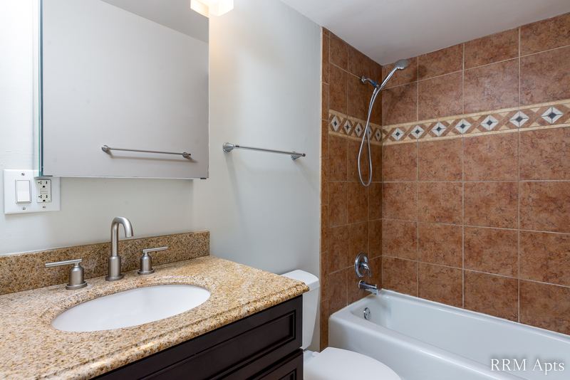 Bathroom with brown tile tub surround, granite-look vanity on dark cabinet and a medicine cabinet, Cook Street apartment 4