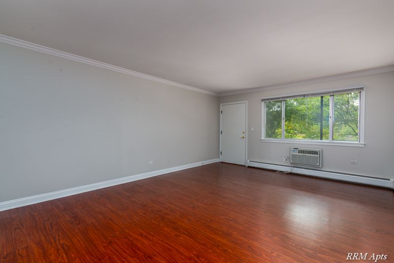 Living room with wood-look floor, window, wall air conditioner and front door, Cook Street apartment 6