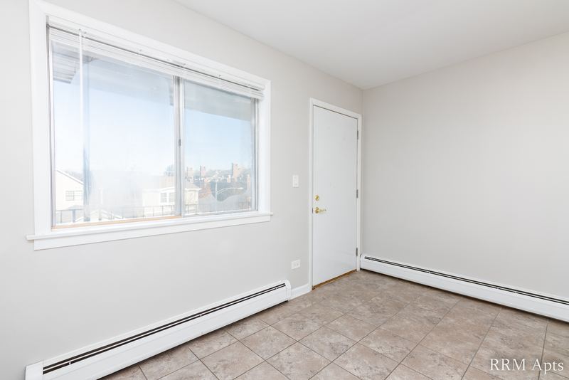Living room with wood floor, wide window with a view of rooftops and a white entry door, Cook Street apartment 9