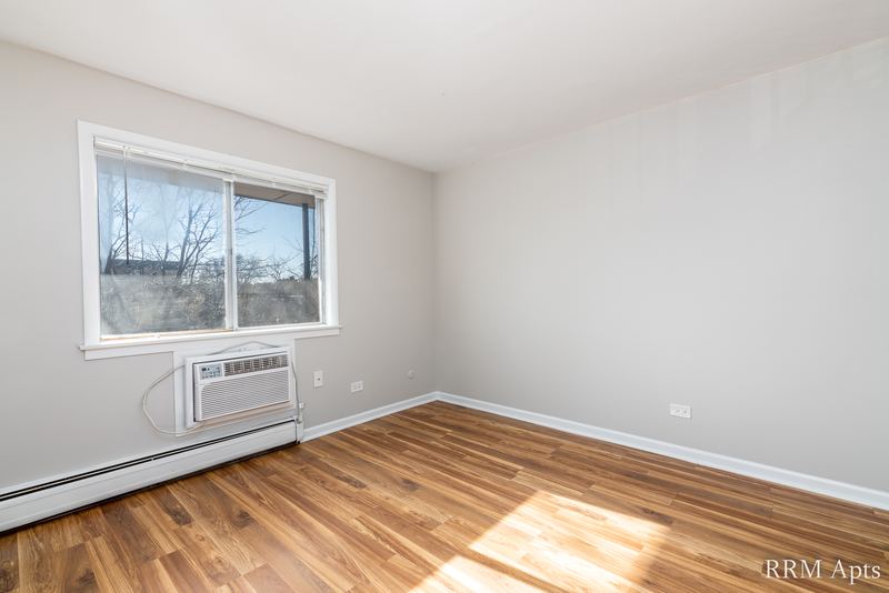 Bedroom with wood floor, one window with a wall air conditioner below it and baseboard radiator, Cook Street apartment 9