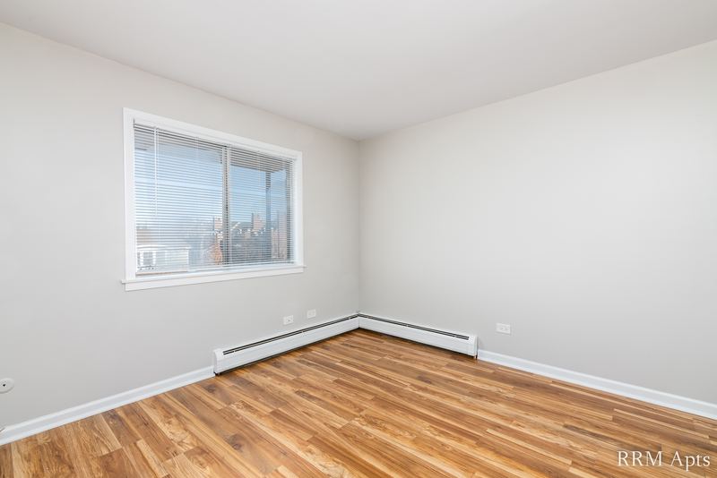 Bedroom with wood floor, a window in the corner and baseboard radiator, Cook Street apartment 9